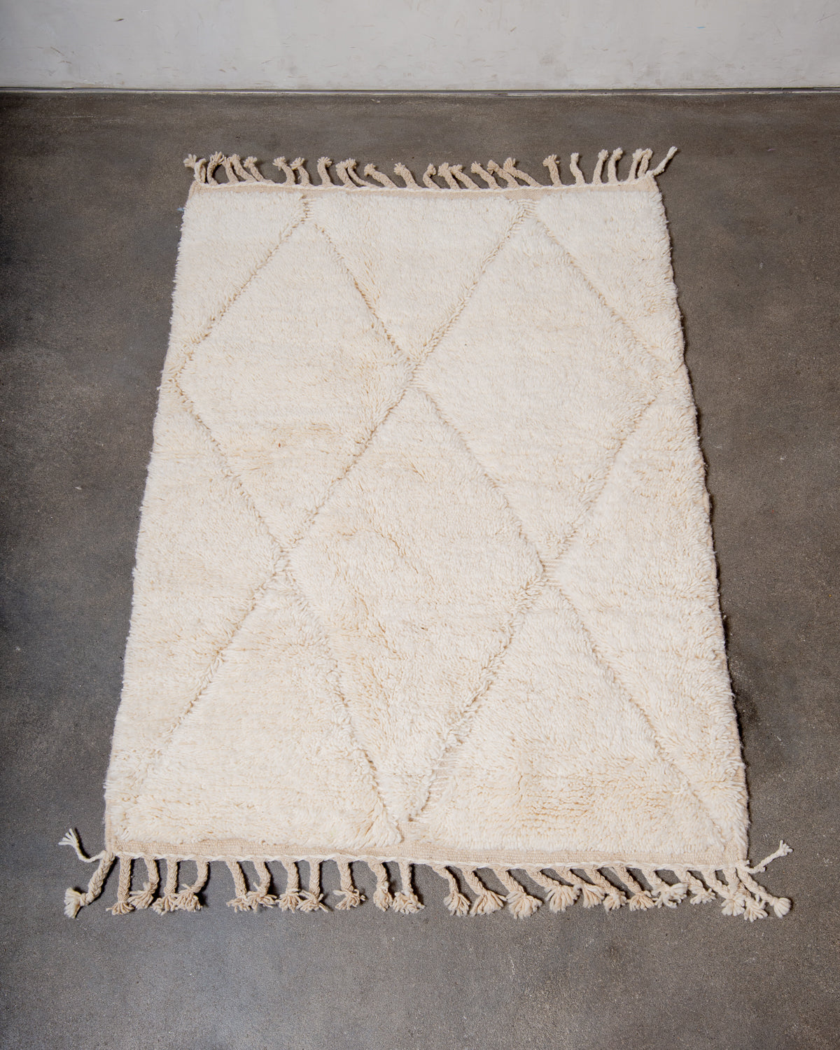 Beniourain rug in cream wool laying on concrete studio floor.